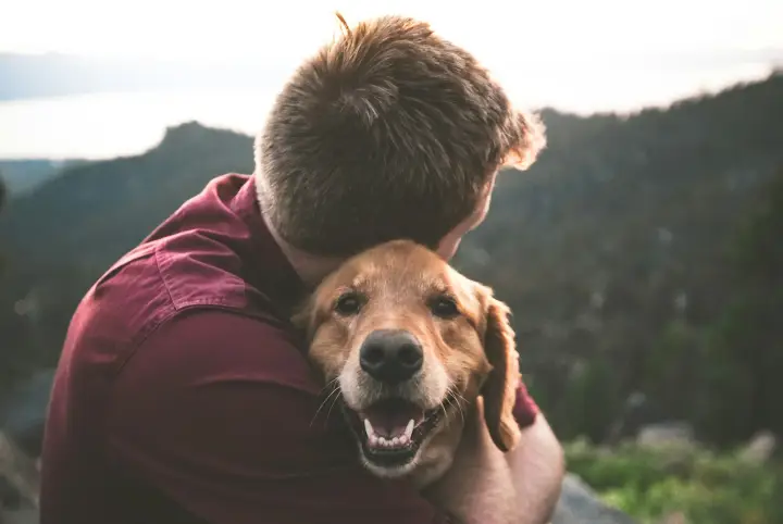 Pet parent hugging a smiling golden dog outdoors